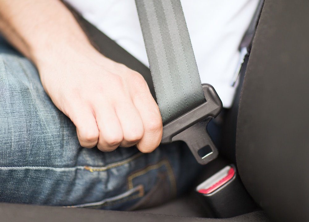 A person is holding the seat belt of their car.