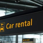 A sign that says car rental in front of an airport terminal.