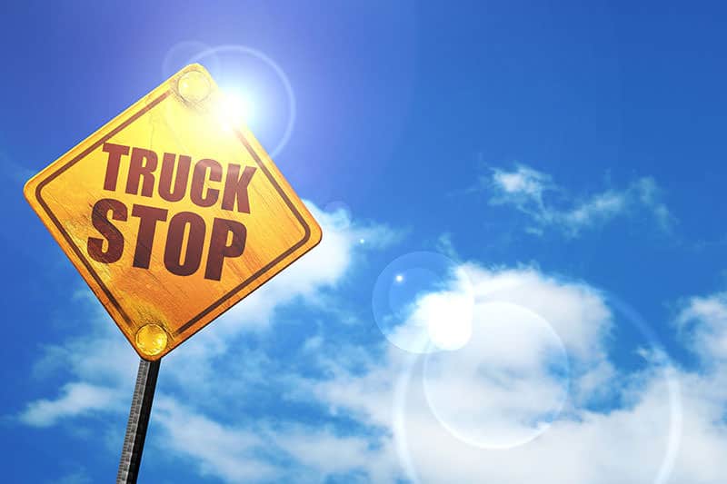 A yellow truck stop sign under a blue sky.