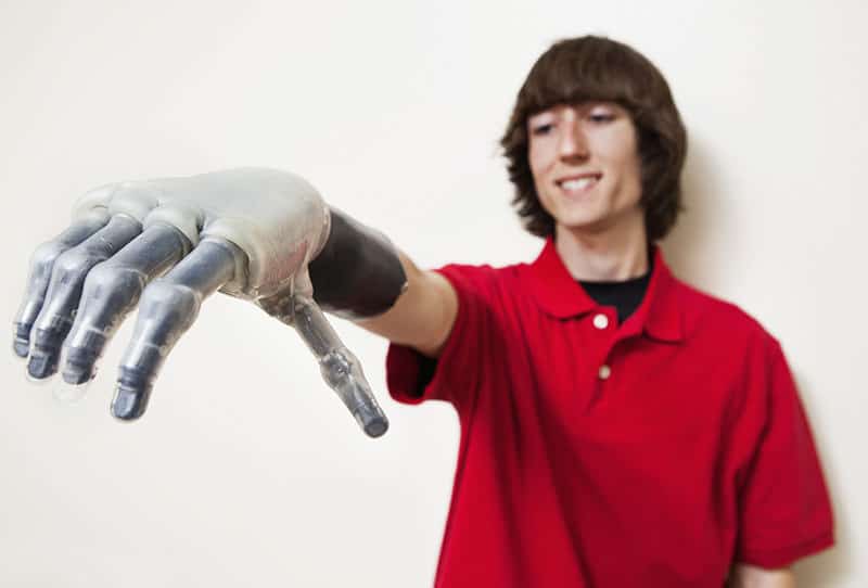 A man in red shirt holding up a robot hand.
