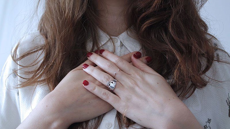 A woman with red nails holding her hands over her chest.